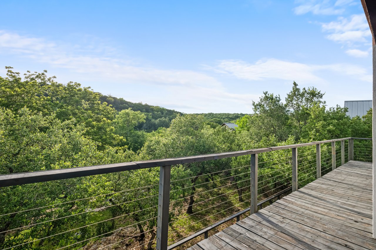 Wooden deck with cable railing overlooking lush woodland and rolling hills.
