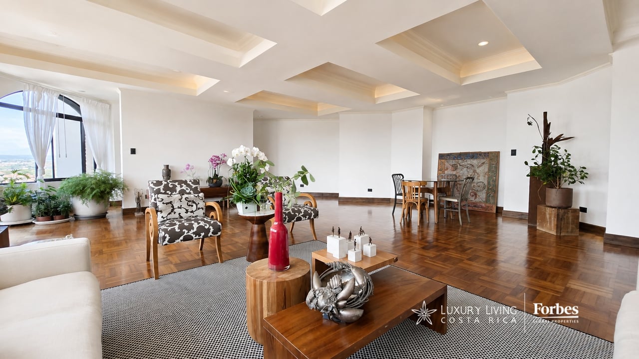 Spacious living and dining area with parquet floors, a recessed ceiling, and a large arched window.