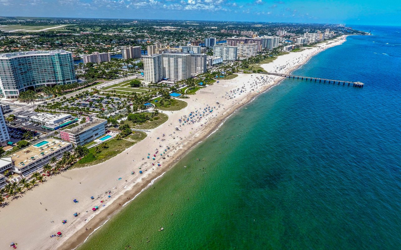 Aerial view of Pompano Beach, with beachfront towers, a sandy shoreline, and a pier.