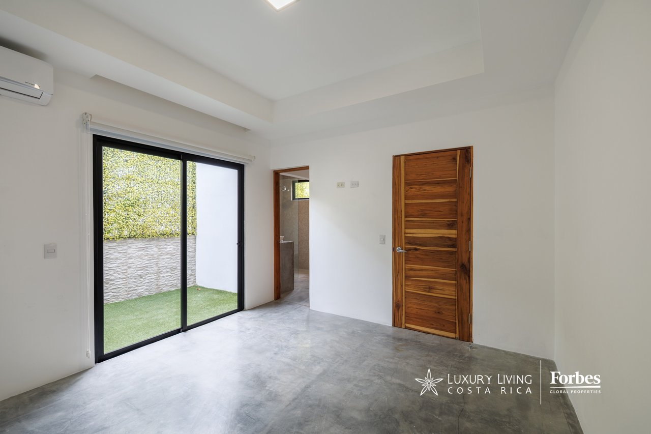 Empty bedroom with concrete flooring and sliding glass doors opening onto a small garden.