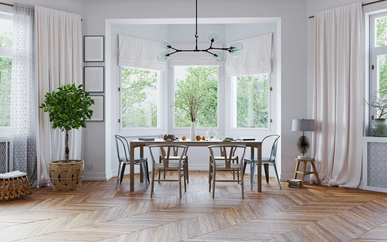 Bright dining room with a wooden table and chairs beneath large curtained windows.