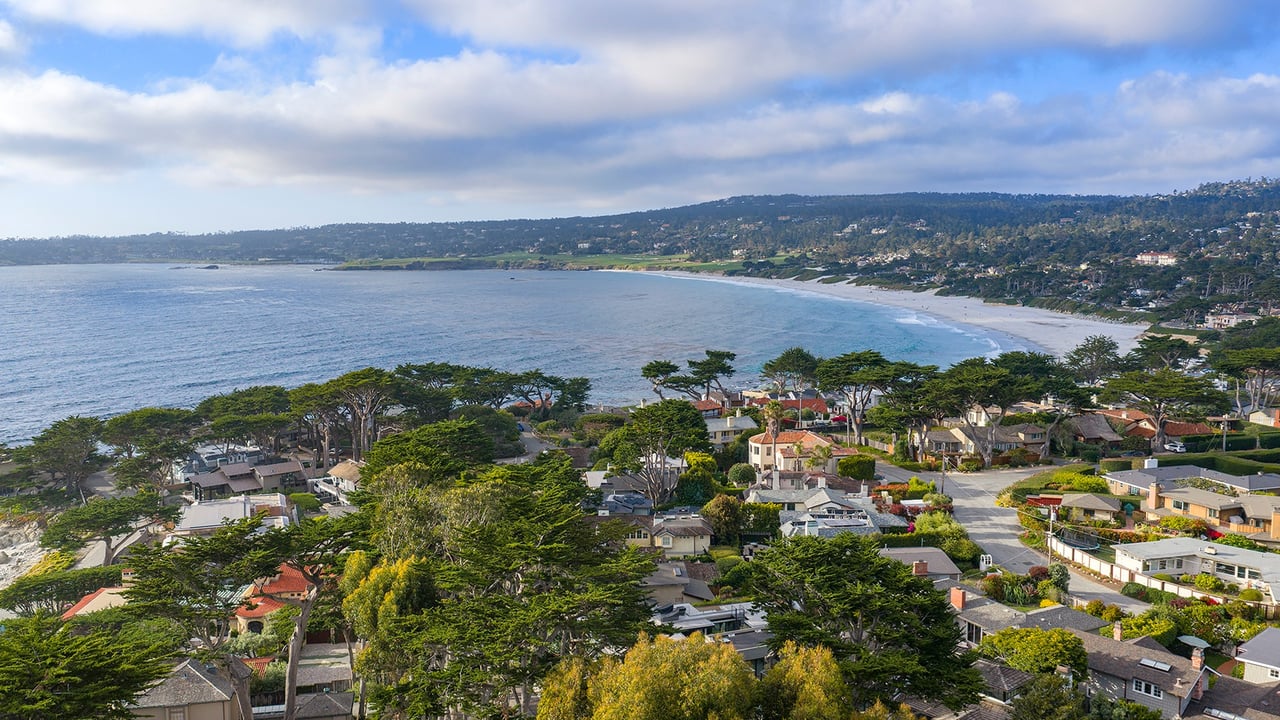 Aerial view of Carmel Point homes beside a curving bay and sandy coastline.
