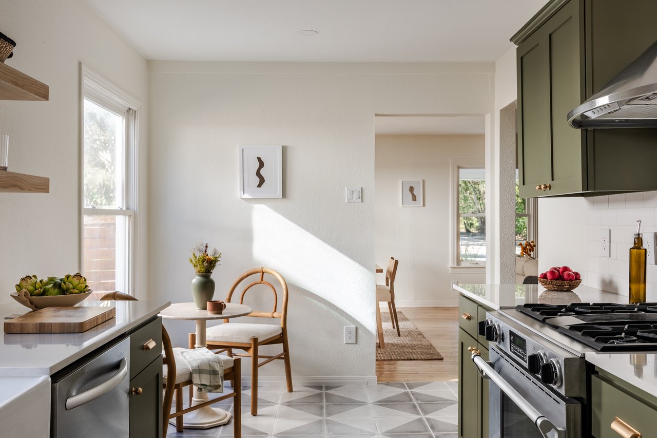 Bright kitchen with green cabinets, stainless range, and a sunlit dining nook.