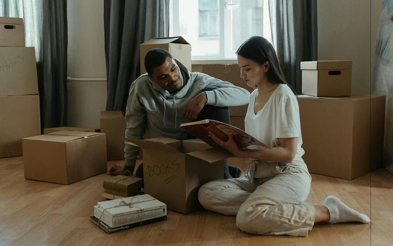 A couple looks through a photo album while packing among moving boxes.