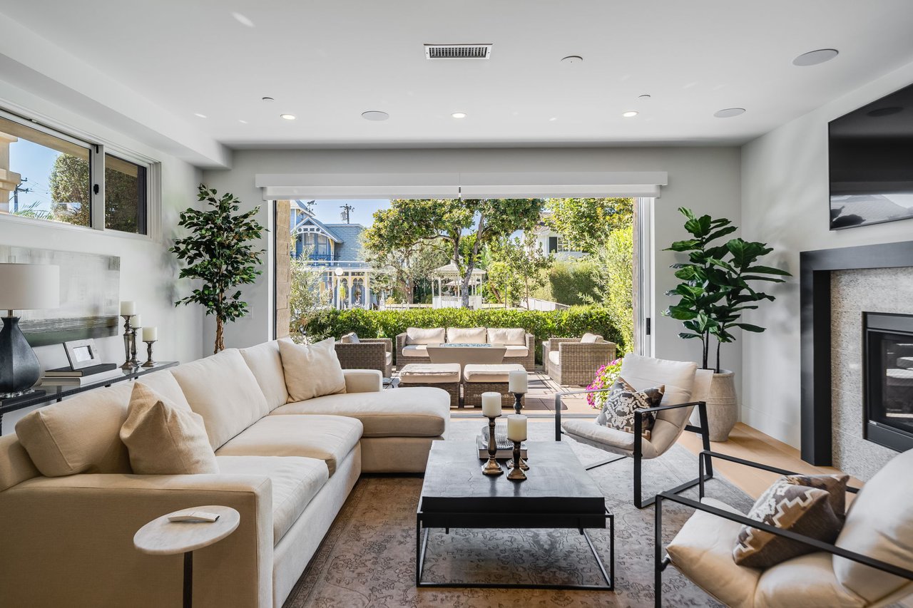 Furnished living room with a cream sectional, fireplace, and wide patio opening overlooking a garden.