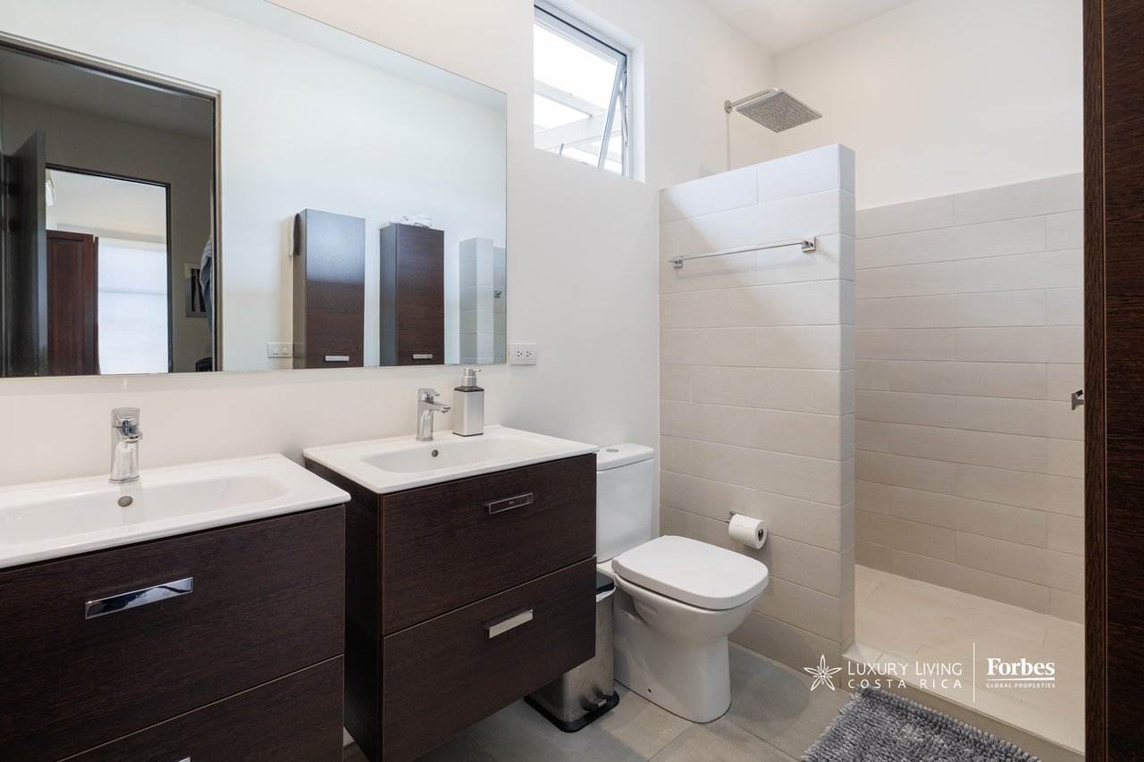 Bathroom with double dark-wood vanities, a large mirror, toilet, and tiled walk-in shower.