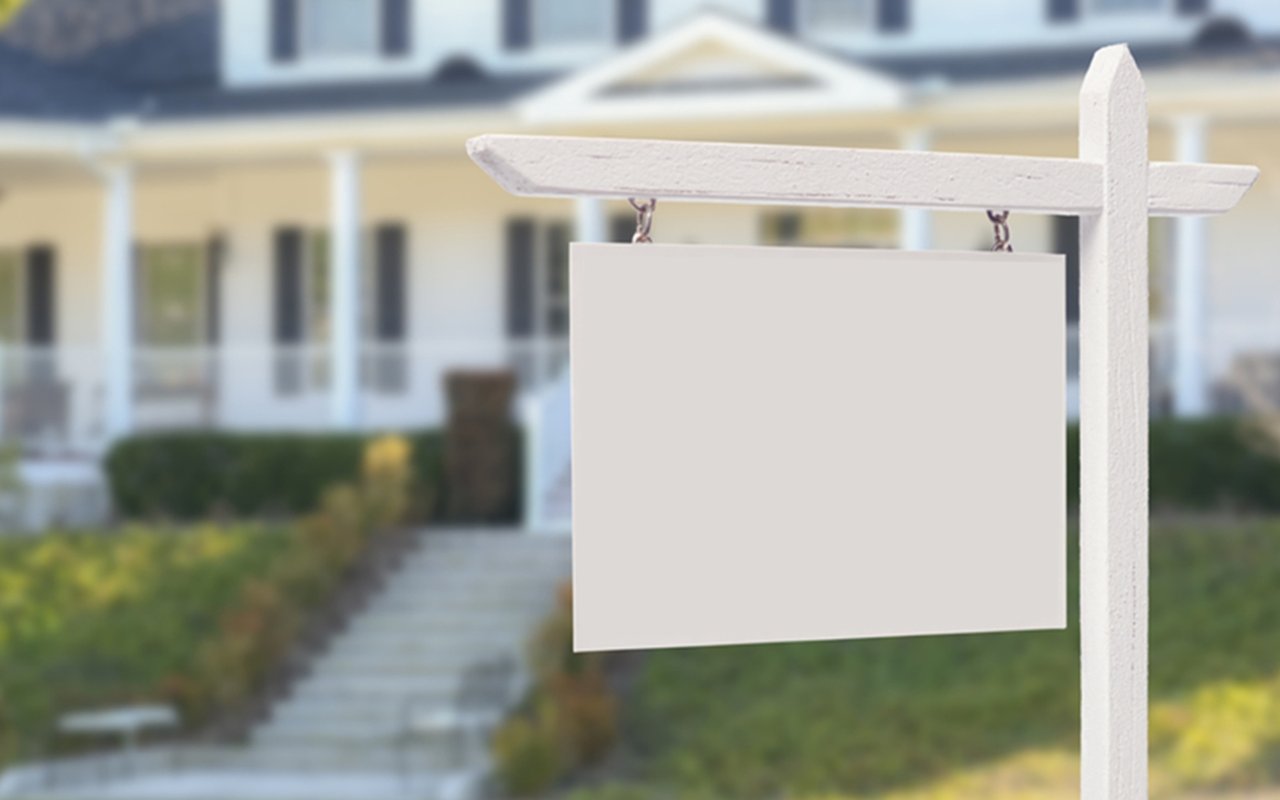 Blank real estate sign in front of a house with a walkway to the porch.