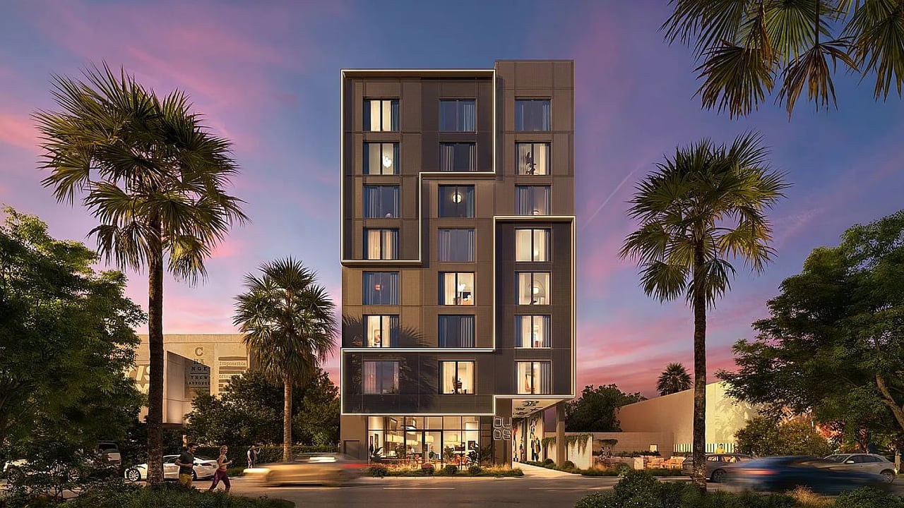 Duos Wynwood’s modern multi-story building at dusk, framed by palm trees.