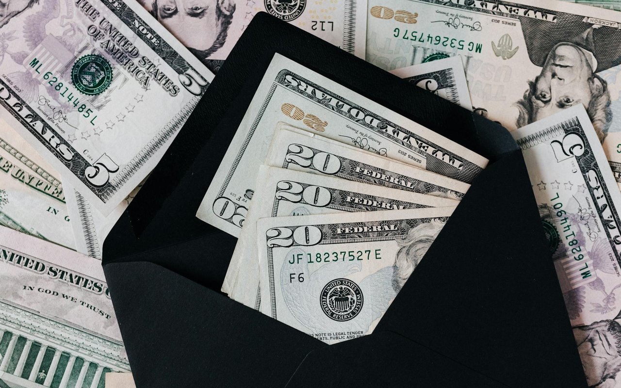 U.S. dollar bills tucked into a black envelope, with more bills scattered beneath.