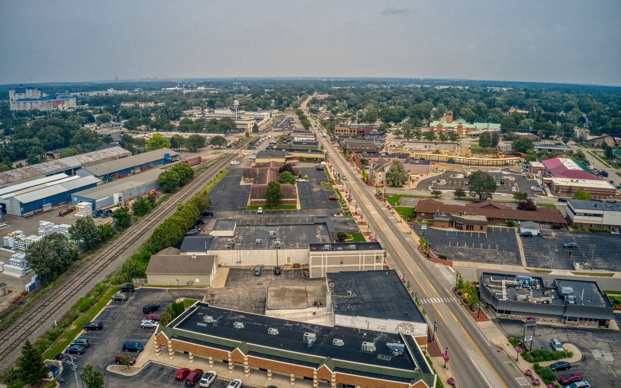 Aerial view of a small town’s commercial district, with railroad tracks and a main road leading toward the horizon.