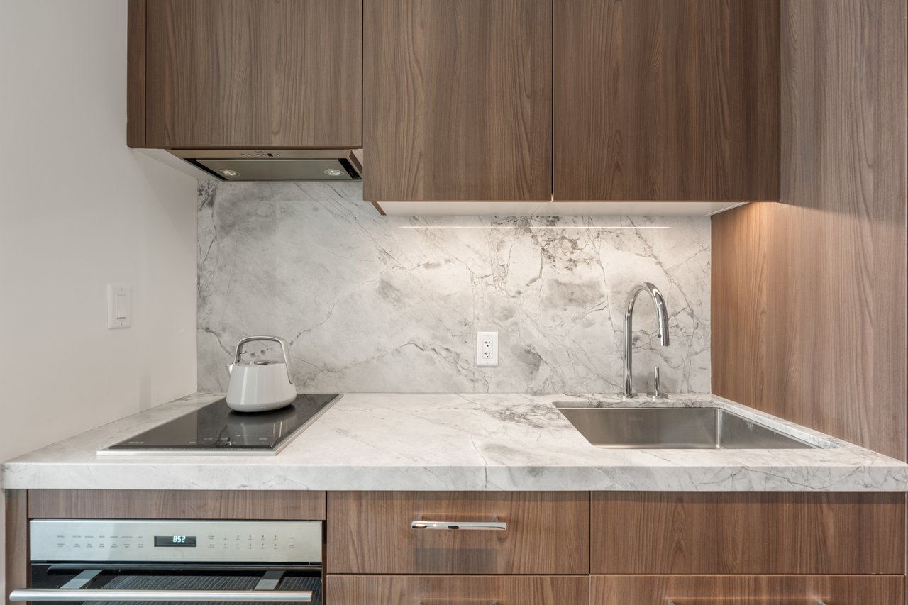 Modern kitchen with veined marble counters, walnut cabinets, induction cooktop, and stainless-steel sink.