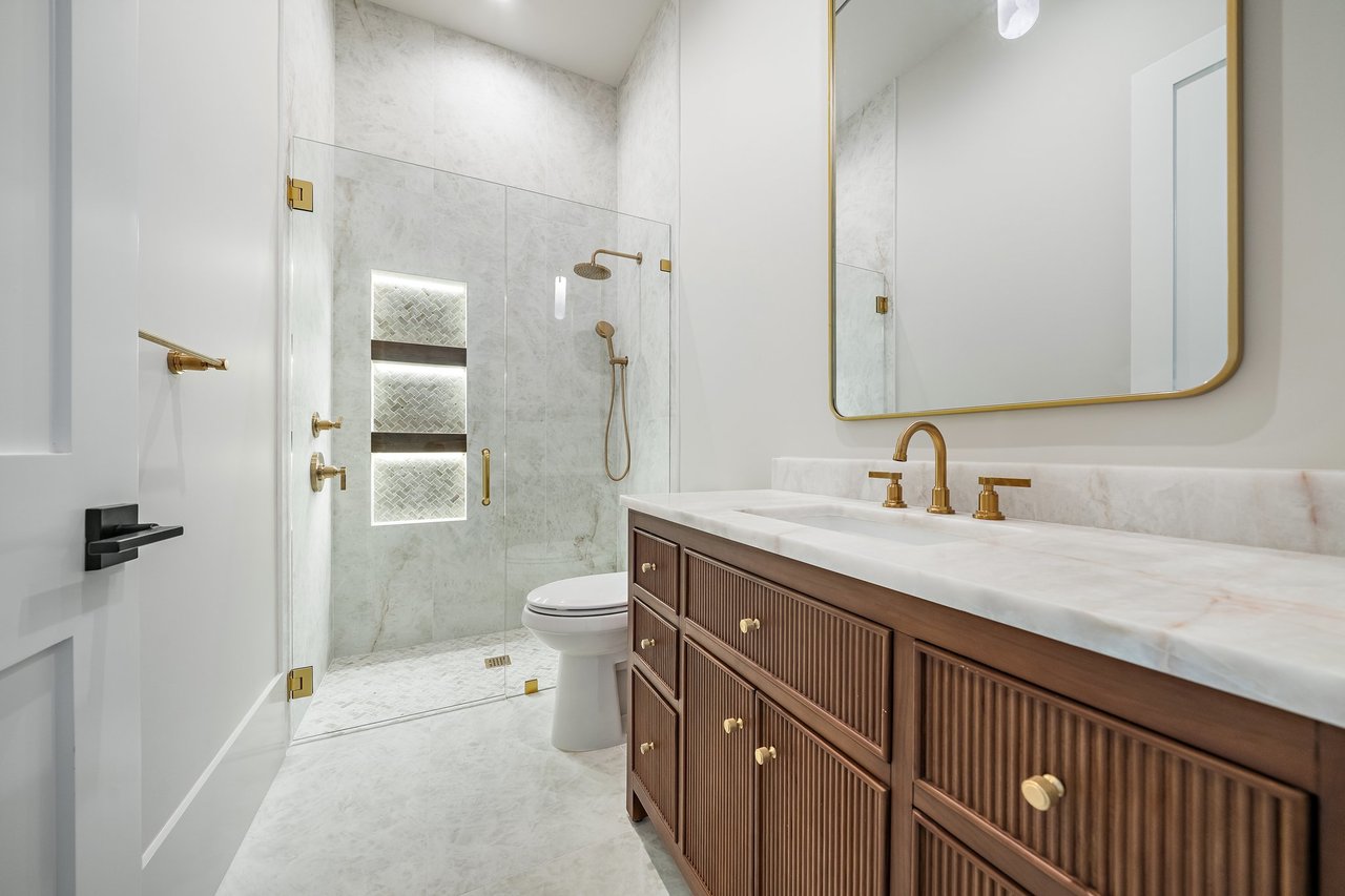 Luxury bathroom with a marble shower, illuminated niche, and ribbed wood vanity with gold fixtures.