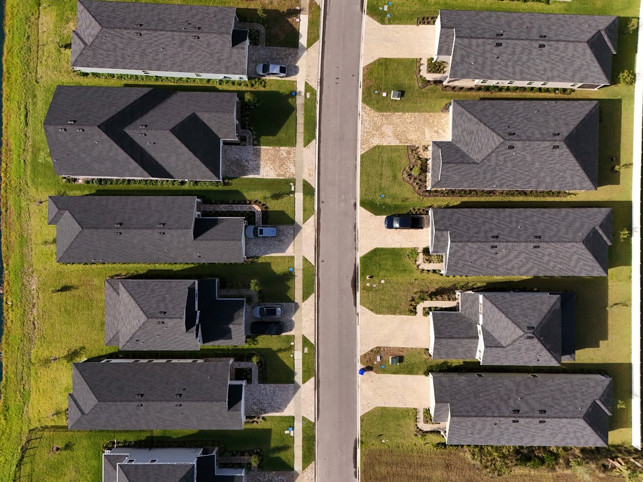 Aerial view of detached homes lining a residential street, with green lawns and driveways.