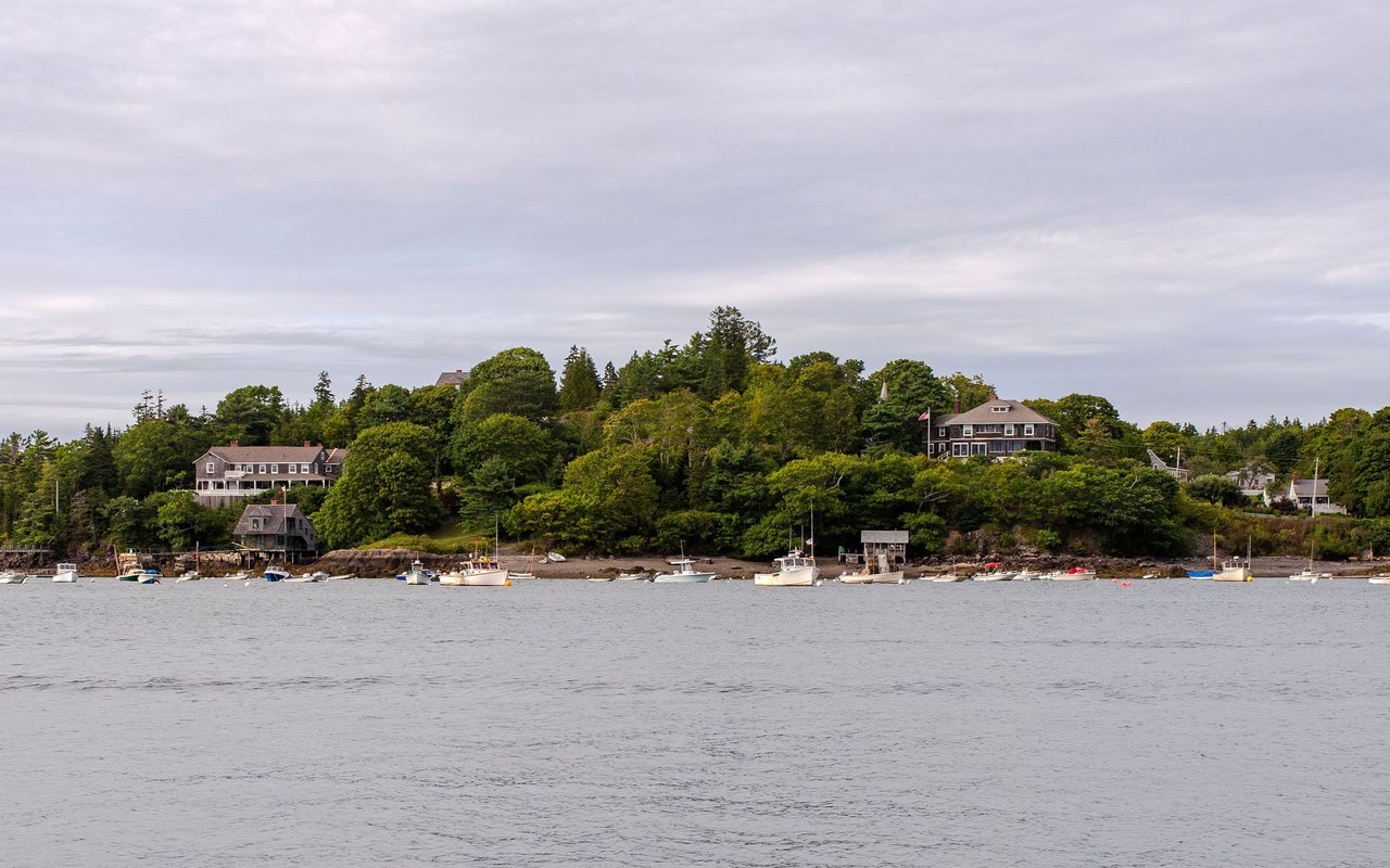 Waterfront homes along a wooded shoreline, with small boats moored in the bay.