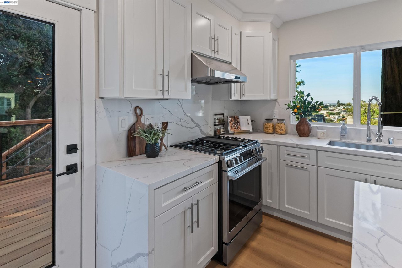 Bright kitchen with white cabinets, veined stone counters, stainless range, and a window overlooking the neighborhood.