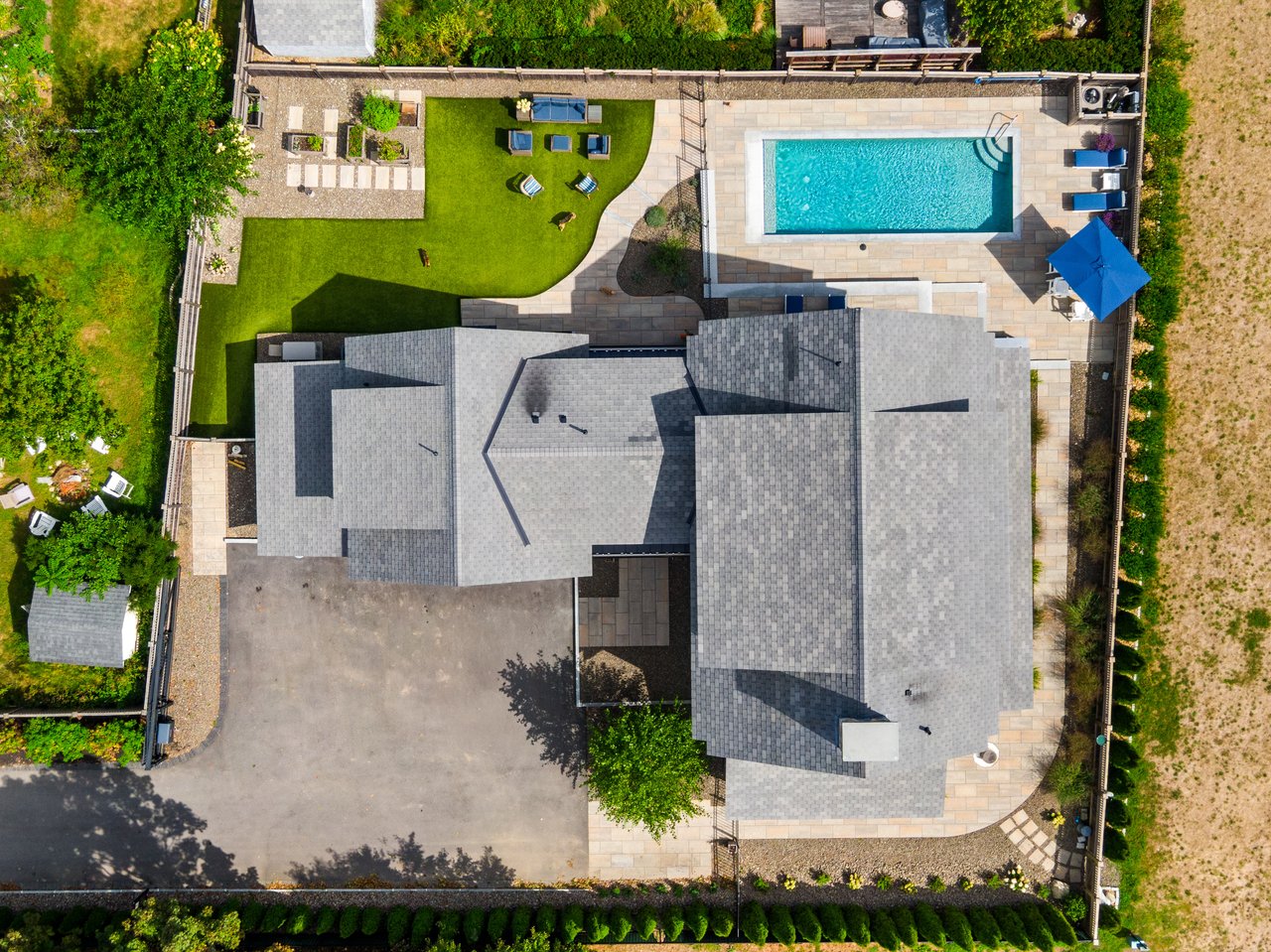 Aerial view of a home with a rectangular pool, stone patio, and landscaped lawn.