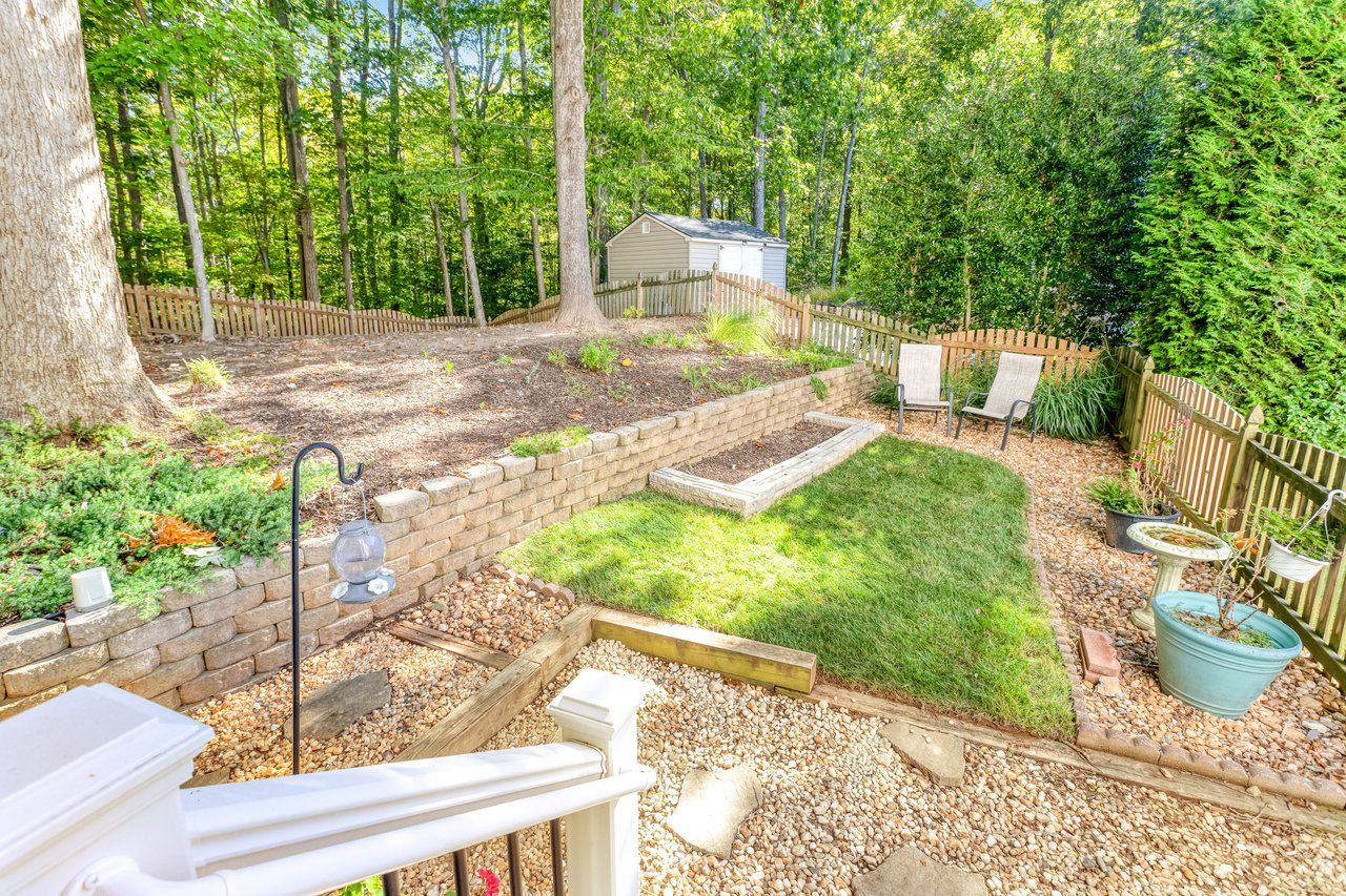 Fenced backyard with a raised stone garden bed, lawn, patio chairs, and a storage shed.