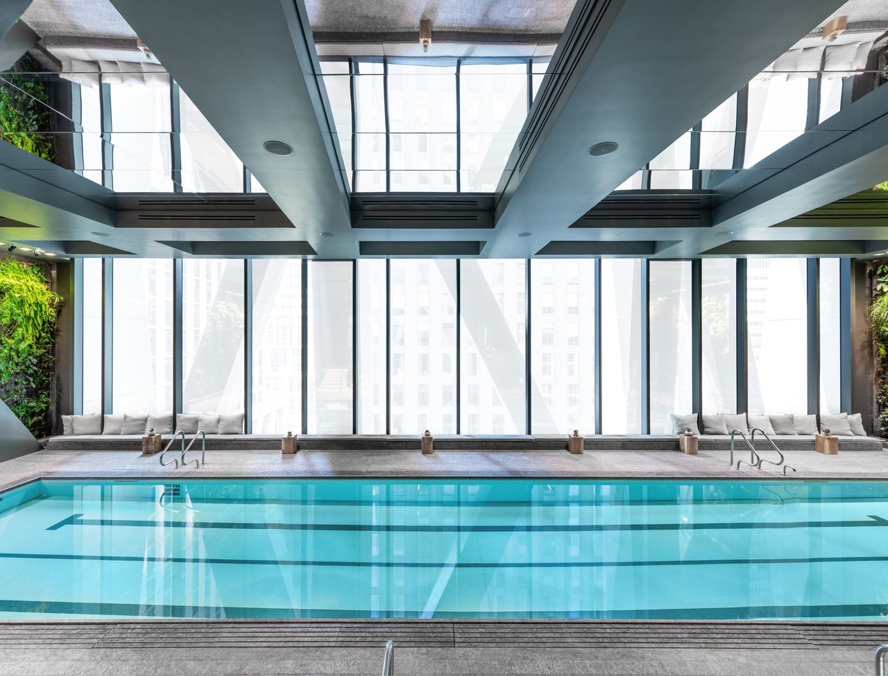 Indoor pool with turquoise lap lanes, floor-to-ceiling windows, and built-in lounge seating.