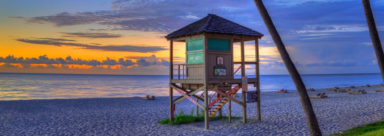 Sunrise over Deerfield Beach, Florida with a lifeguard tower and calm ocean waves.