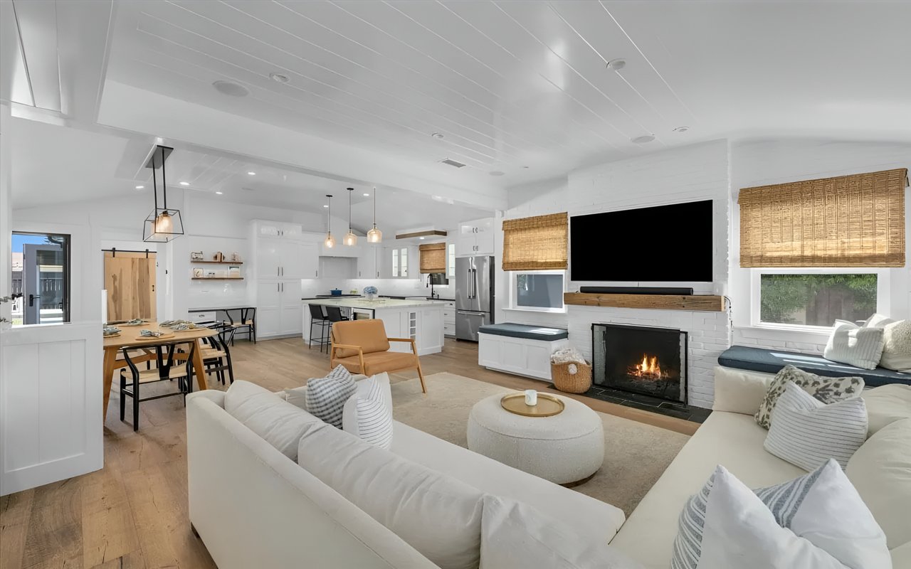  A bright open-concept living room with a fireplace, a white sofa, and a dining area connected to a modern kitchen.