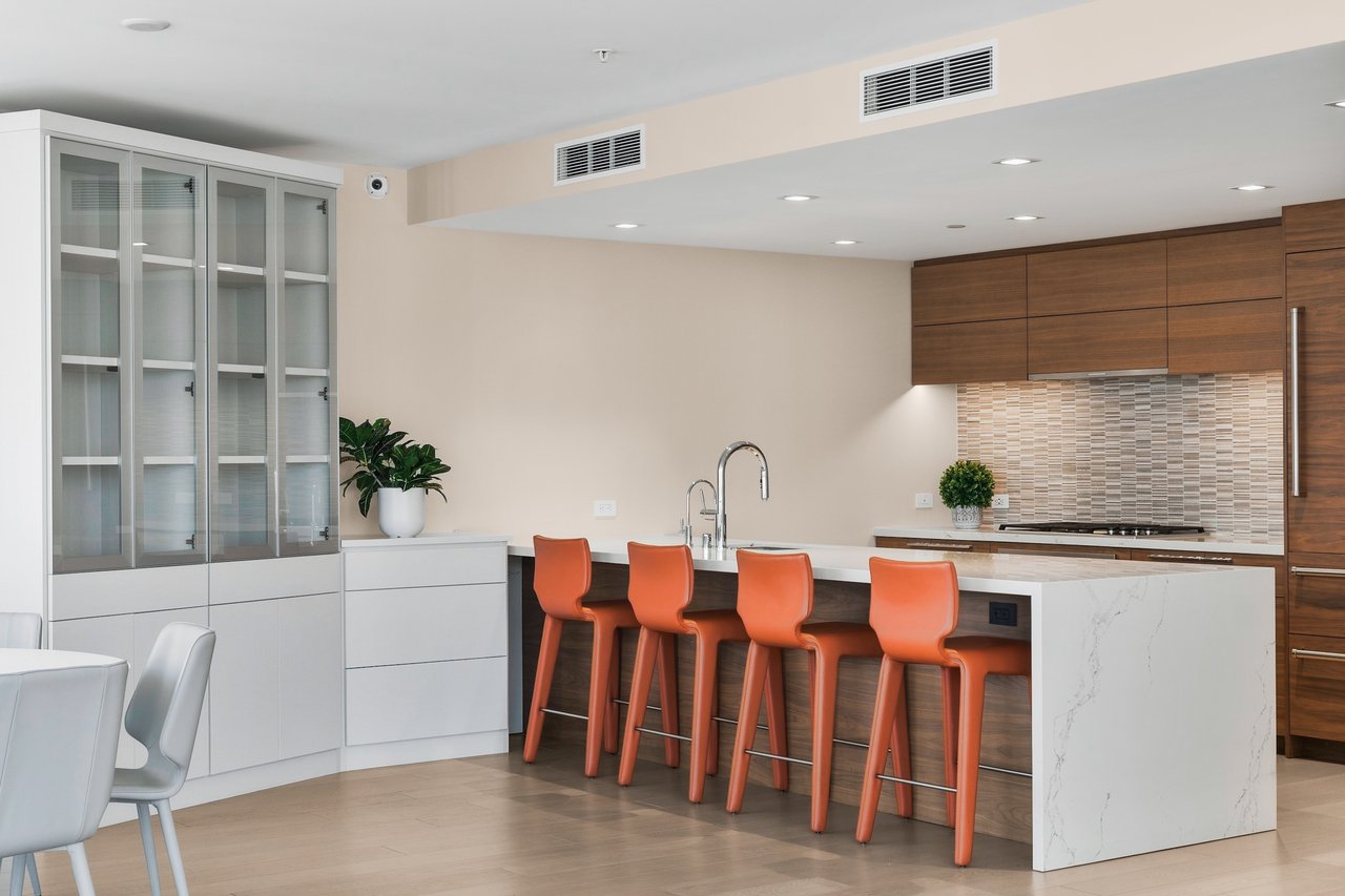 Modern kitchen with a marble island, four orange stools, and dark wood cabinetry.