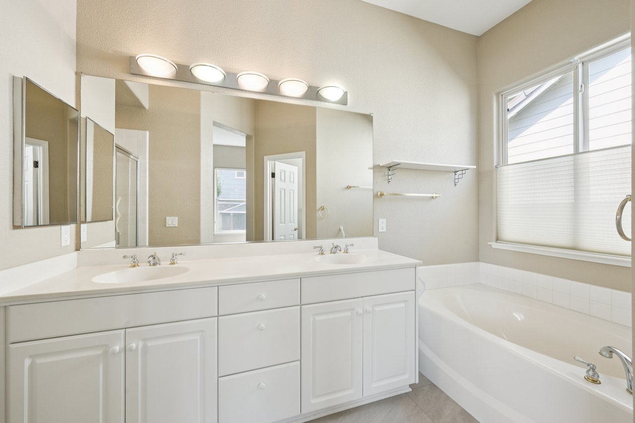 Bathroom with a double-sink vanity and bathtub beneath a wide window.