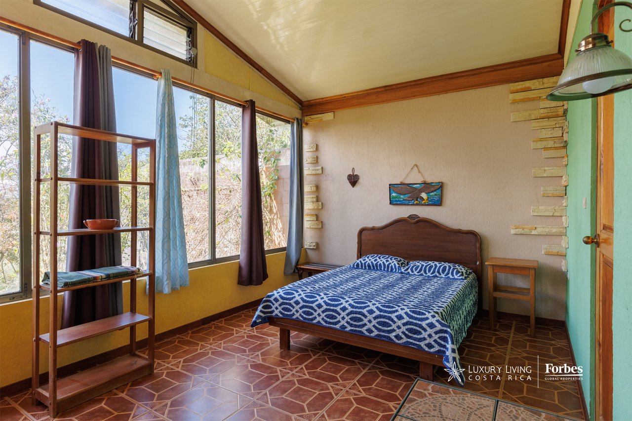 Bedroom with blue patterned bedding, tall curtained windows, and terracotta geometric floor tiles.