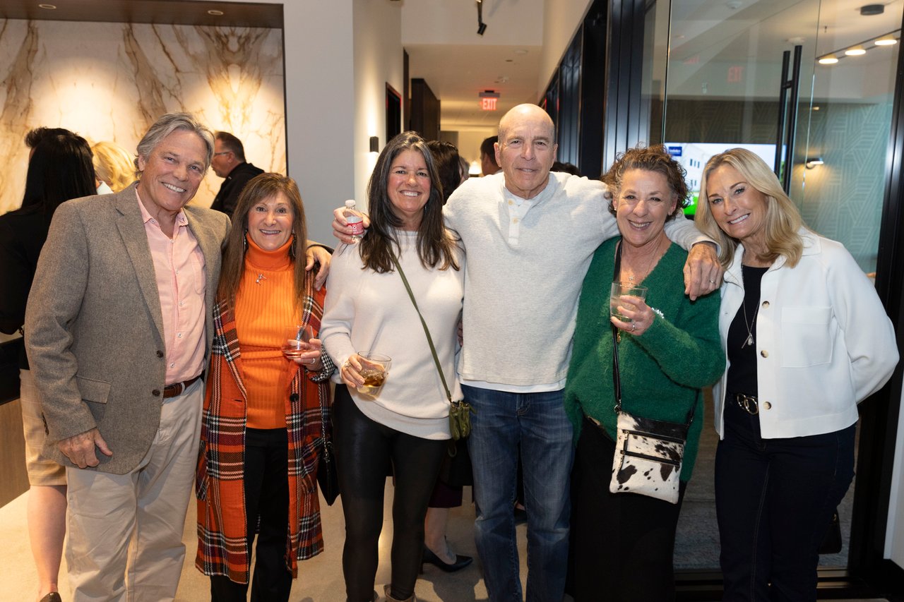 Six adults pose together at an open house, several holding drinks.