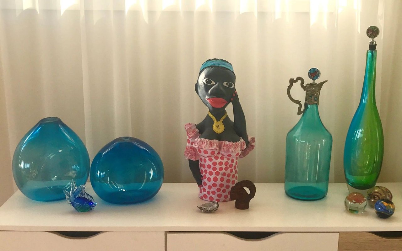 Murano-style glass vases and ornaments displayed beside a figurine in a pink polka-dot dress.