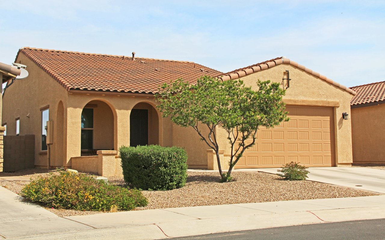 Tan stucco home with a terracotta tile roof, arched entry, two-car garage, and desert landscaping.