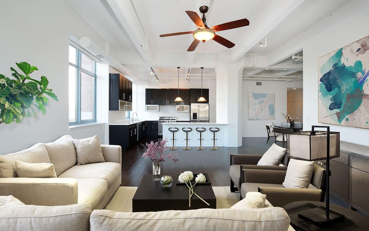 Open-plan loft living room and kitchen with dark cabinetry, a breakfast bar, and large windows.