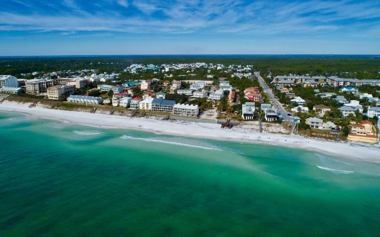 An aerial view of a coastal town with a long stretch of white sand beach and clear, turquoise water.