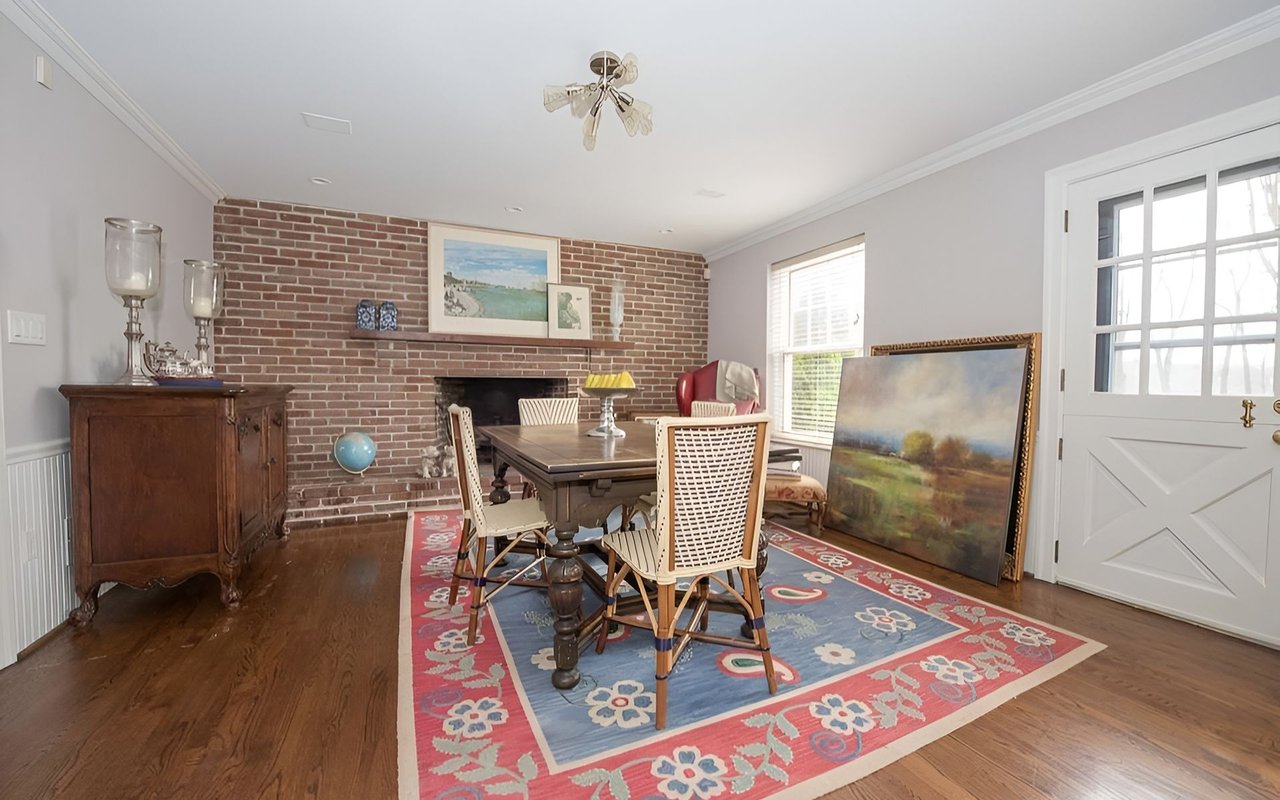 Dining room with a brick fireplace, dark wood table, and colorful patterned rug.