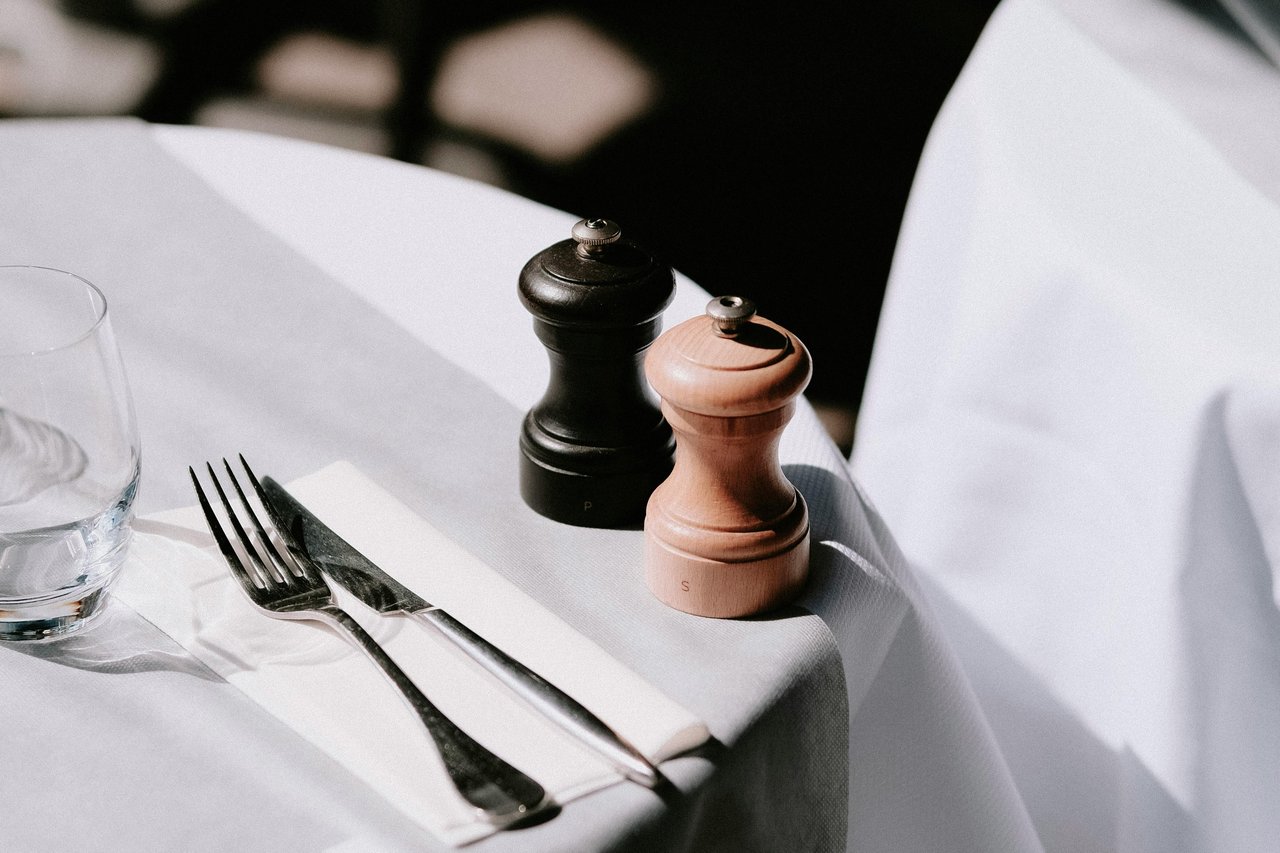 A refined table setup featuring salt and pepper mills, cutlery, and a glass on a white tablecloth, representing upscale dining experiences in the San Fernando Valley.