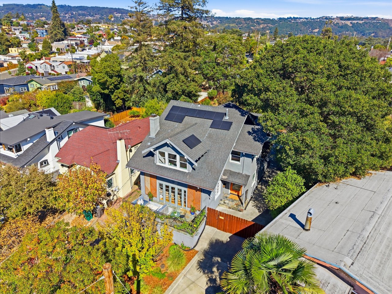 Aerial view of a gray-roofed home with solar panels, landscaped yard, and hillside neighborhood beyond.