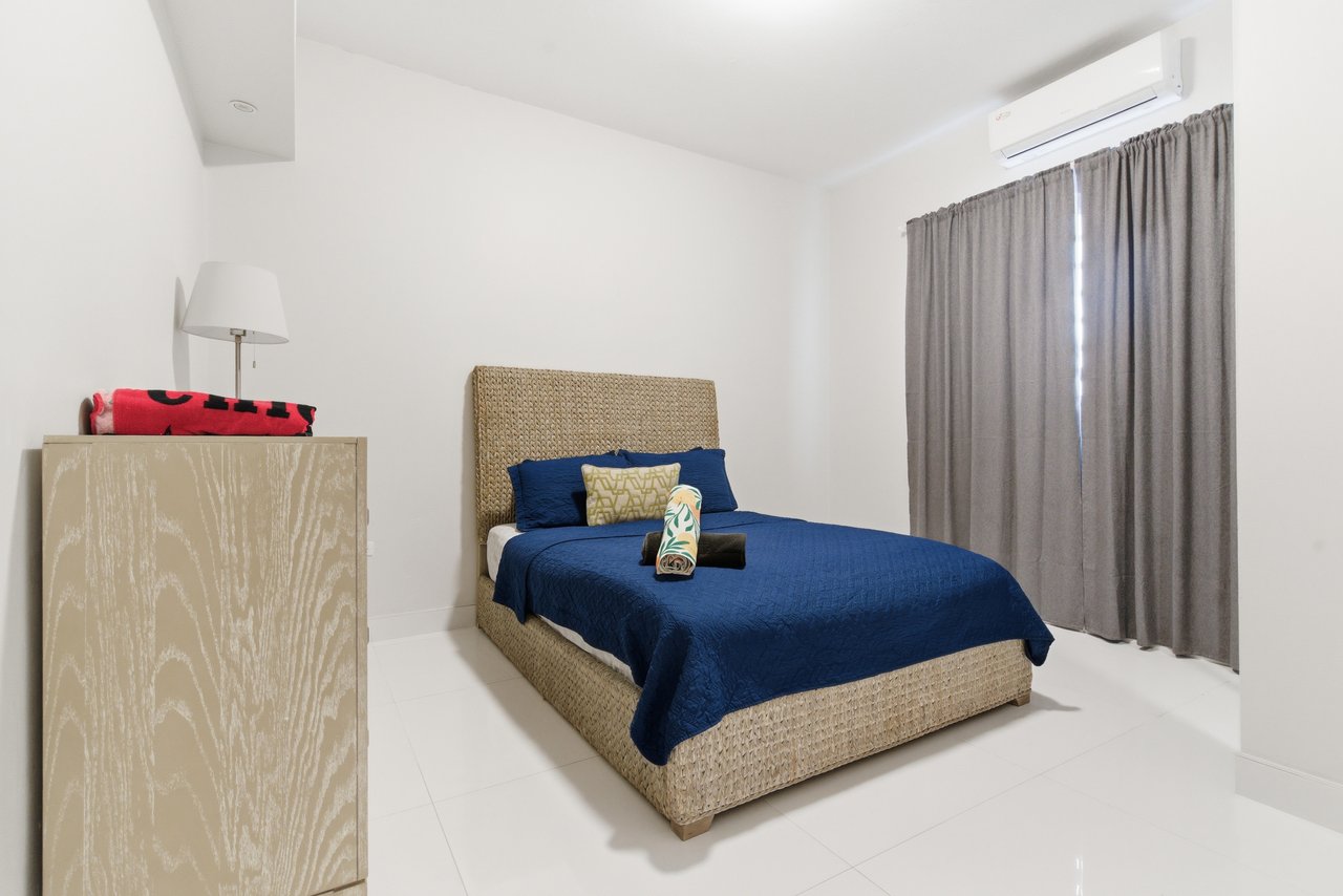 Bedroom with a woven bed frame, navy bedding, gray curtains, and a wall-mounted air conditioner.