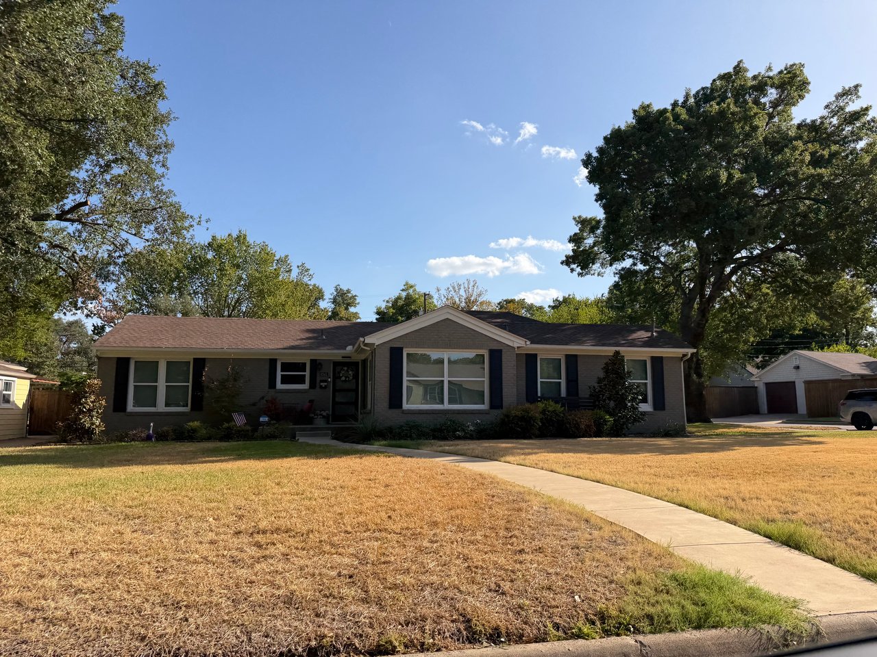 Single-story brick ranch home with a broad dry lawn and curved walkway to the entrance.