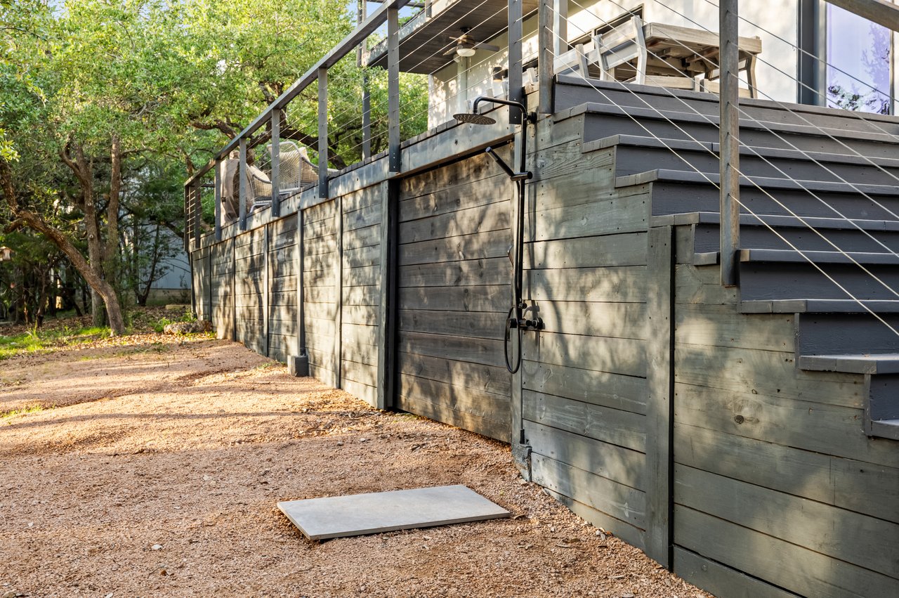 Raised gray-sided deck with broad steps and an outdoor shower beside a gravel yard.