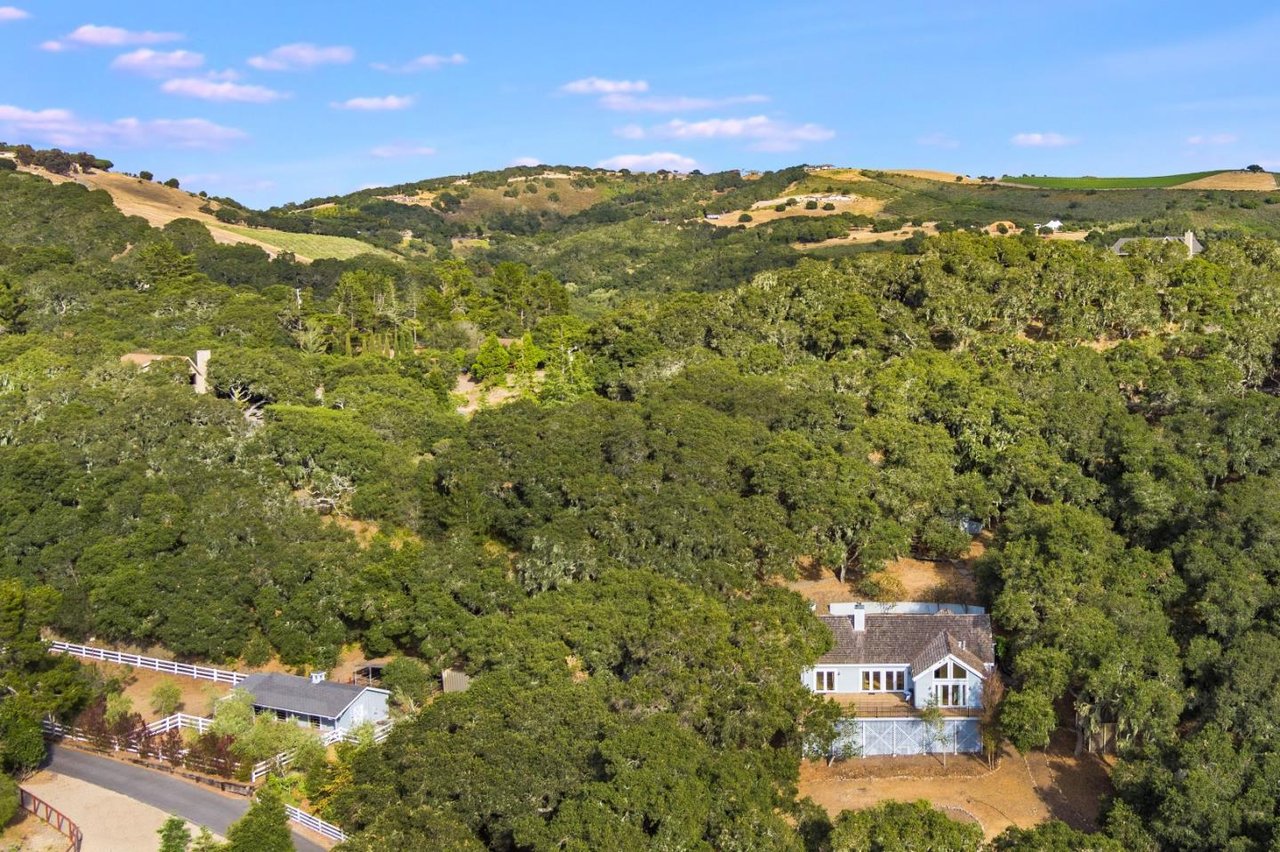 Aerial view of homes among wooded hills, with white fences and golden ridgelines.
