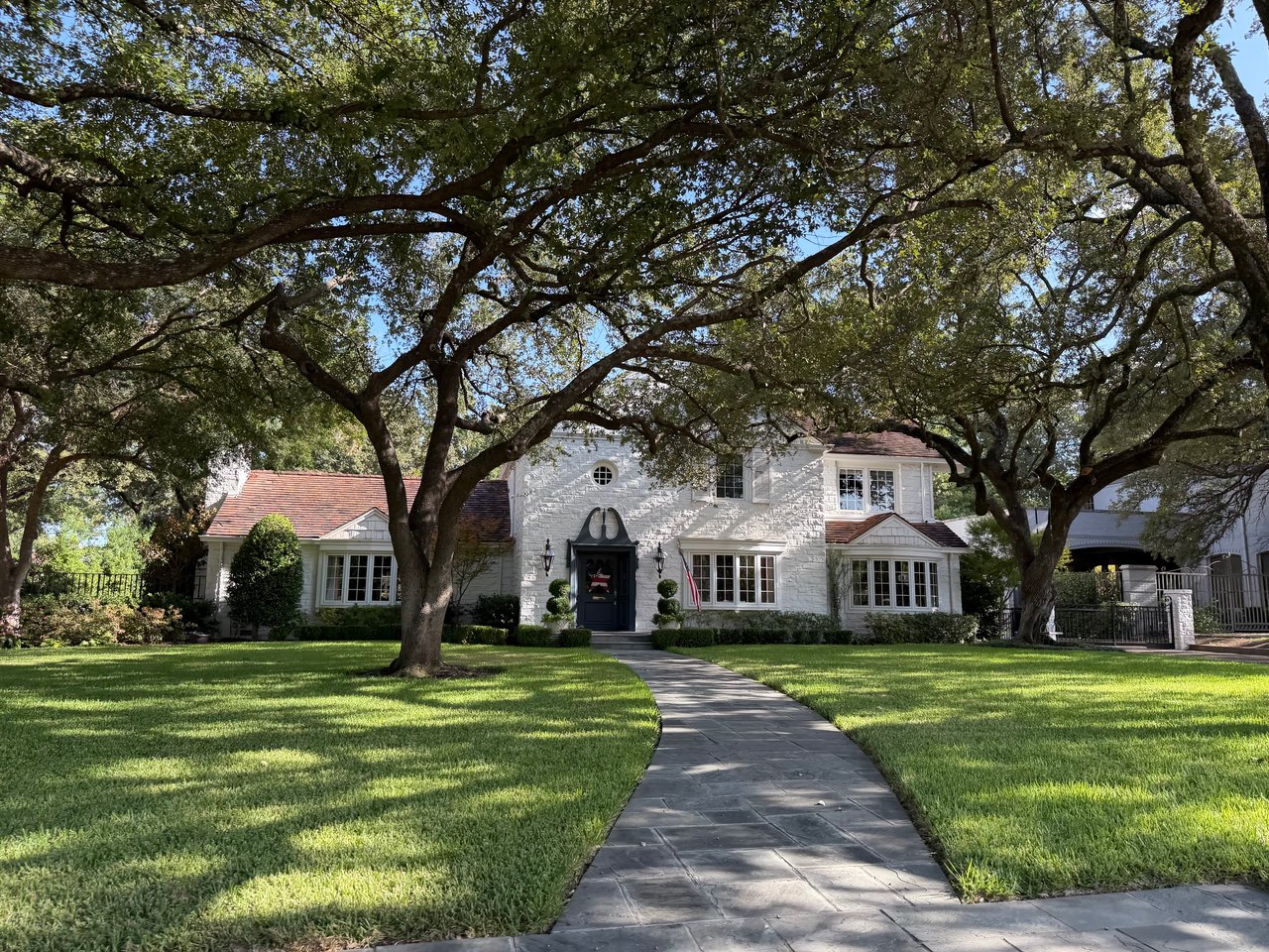 White two-story home framed by mature oak trees, with a curved stone walkway across the lawn.