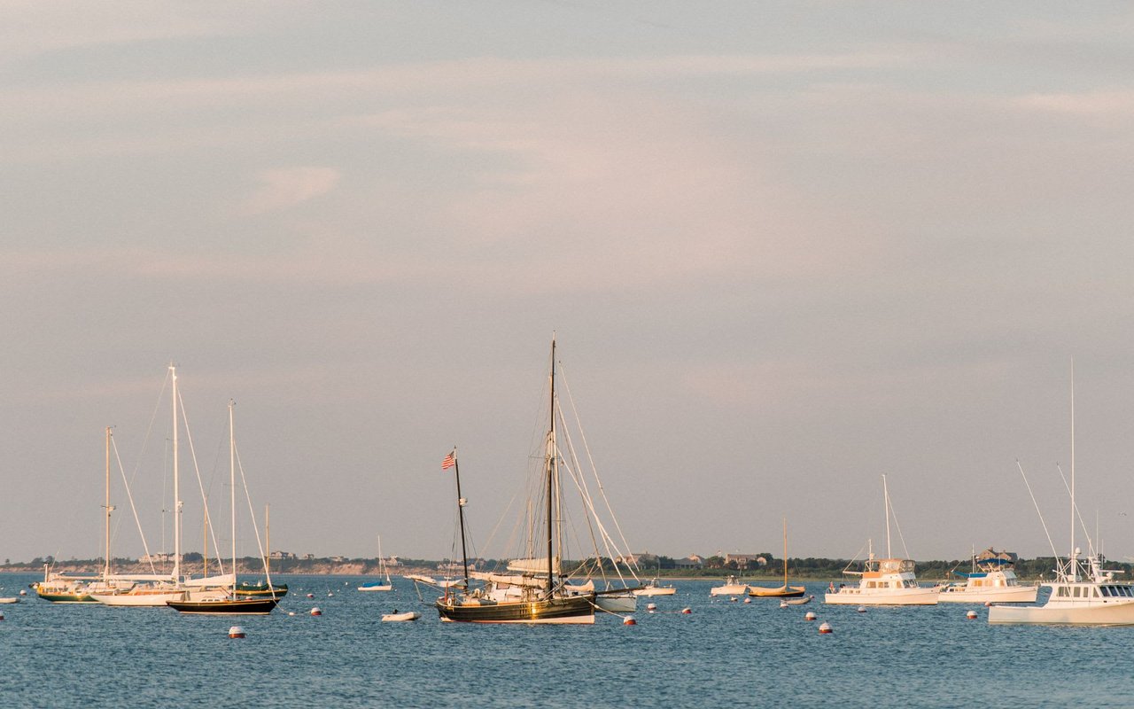 Sailboats floating in the ocean close to shore on a cloudy day in Monomoy.