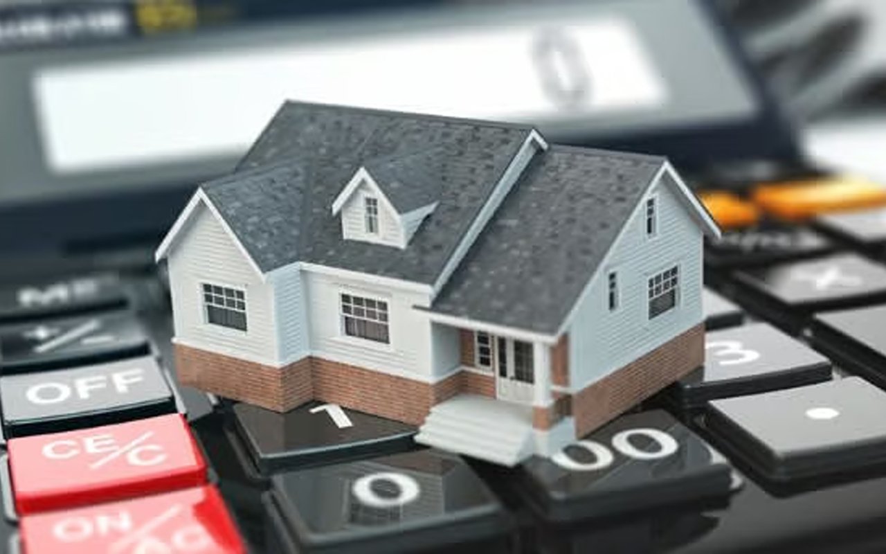A miniature white-and-brick house sits on a calculator, illustrating home mortgage refinancing.