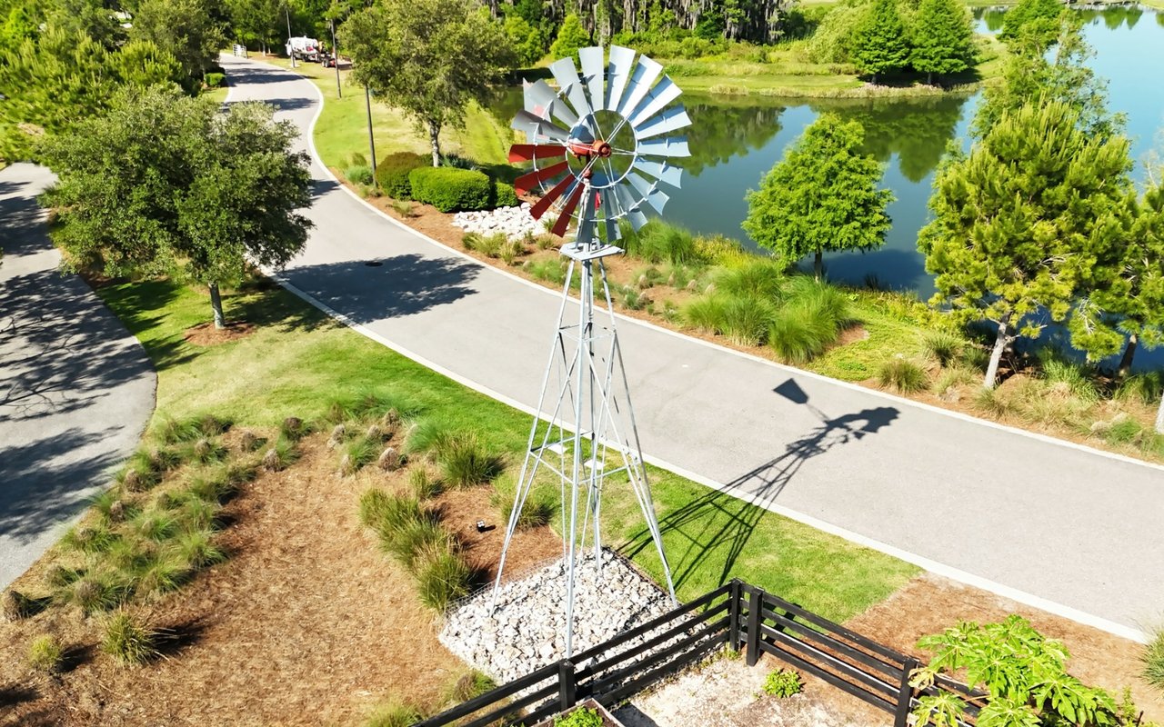 Neighborhood windmill beside a pond and curving roads, surrounded by trees and landscaped grounds.