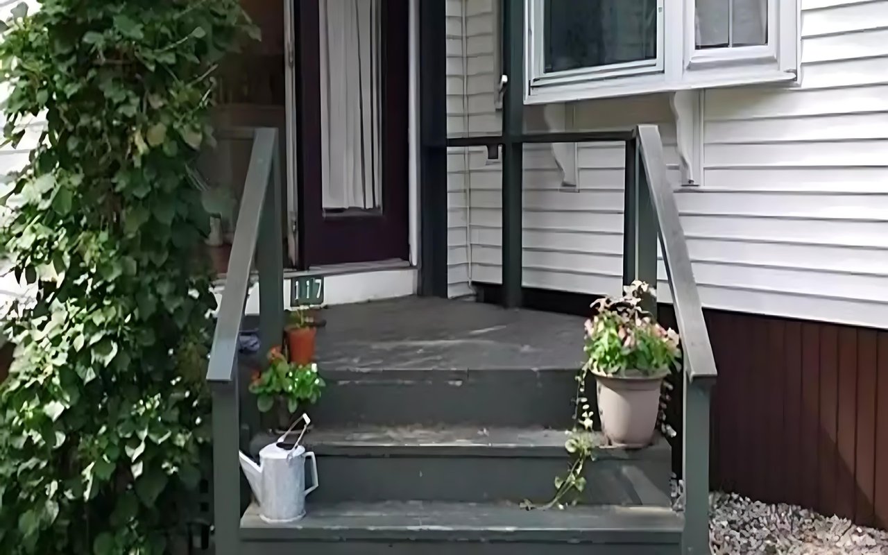 Cottage entrance with green steps, potted plants, and a burgundy front door.