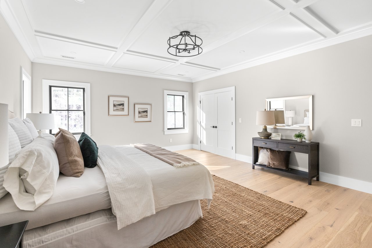 Bright staged bedroom with a coffered ceiling, two windows, and neutral bedding.
