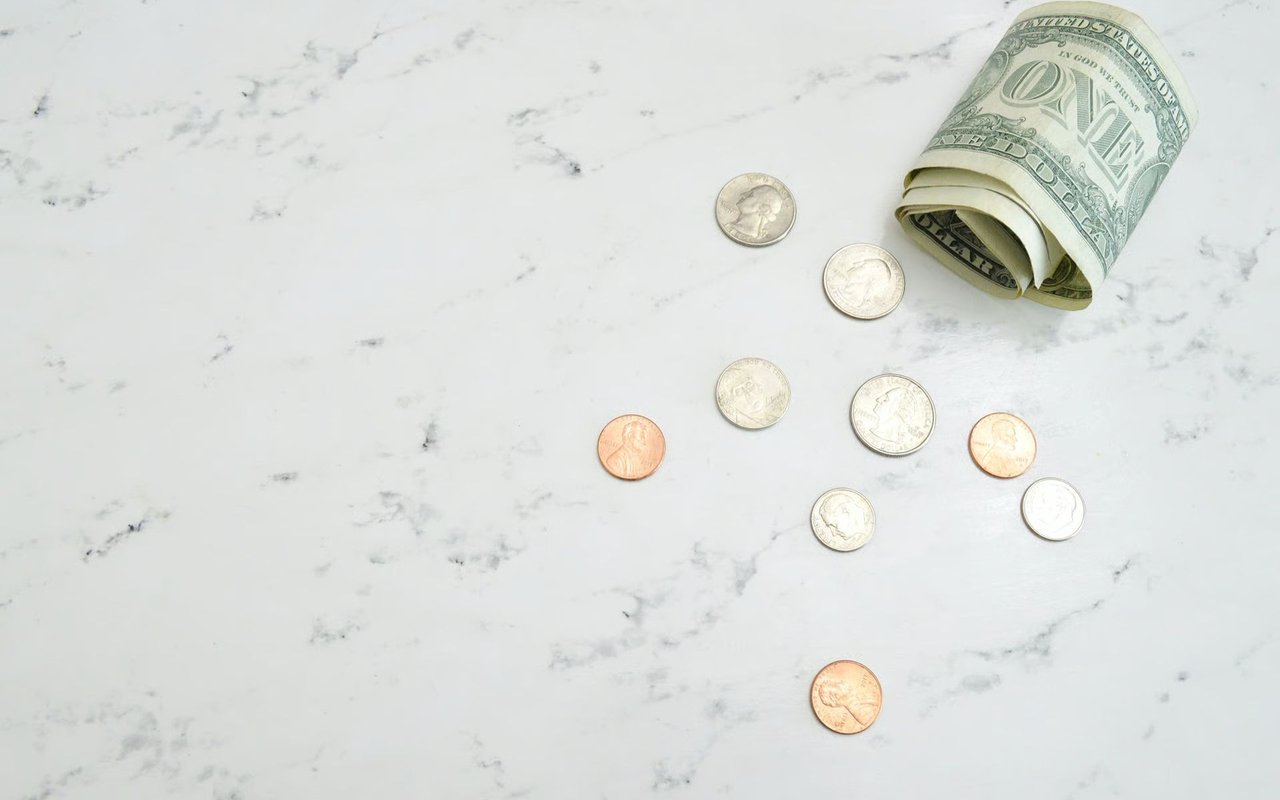 A rolled dollar bill and scattered coins on a white marble surface.