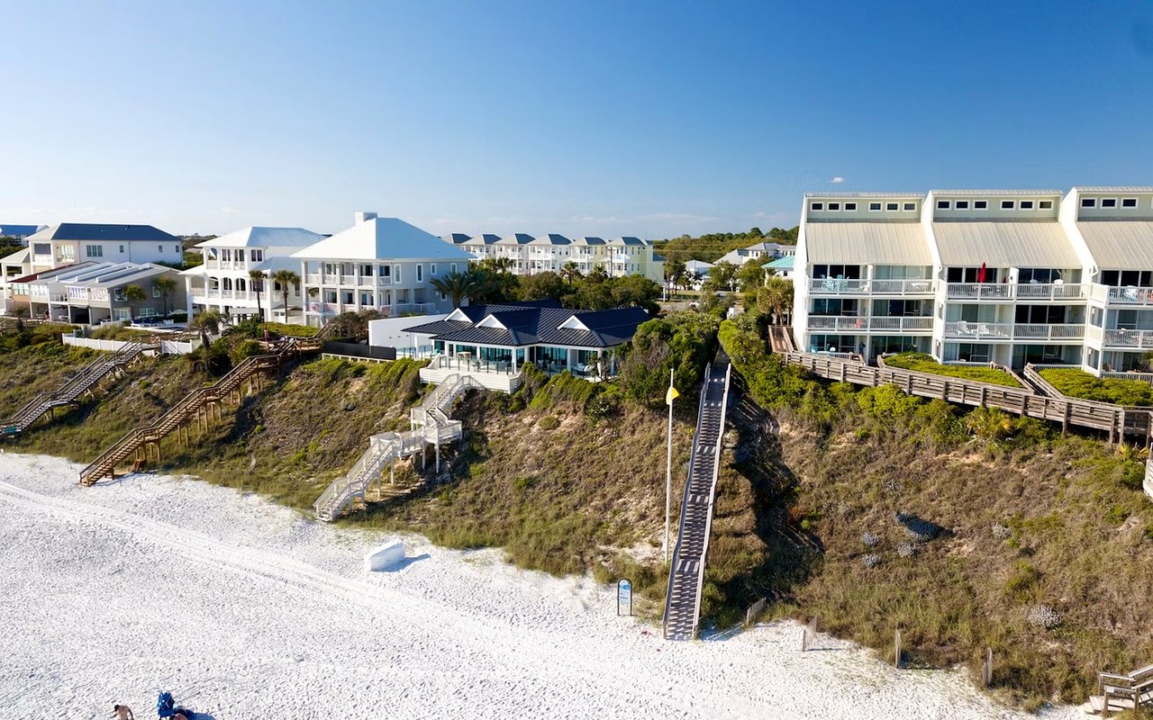 Beachfront homes above a white-sand beach, with wooden stairs crossing the dunes.