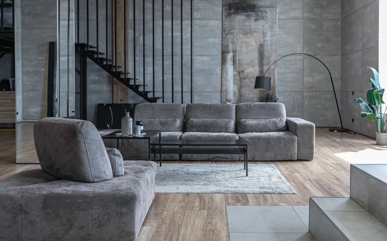  A minimalist living room with a gray sectional sofa, a black coffee table, and a staircase in the background.
