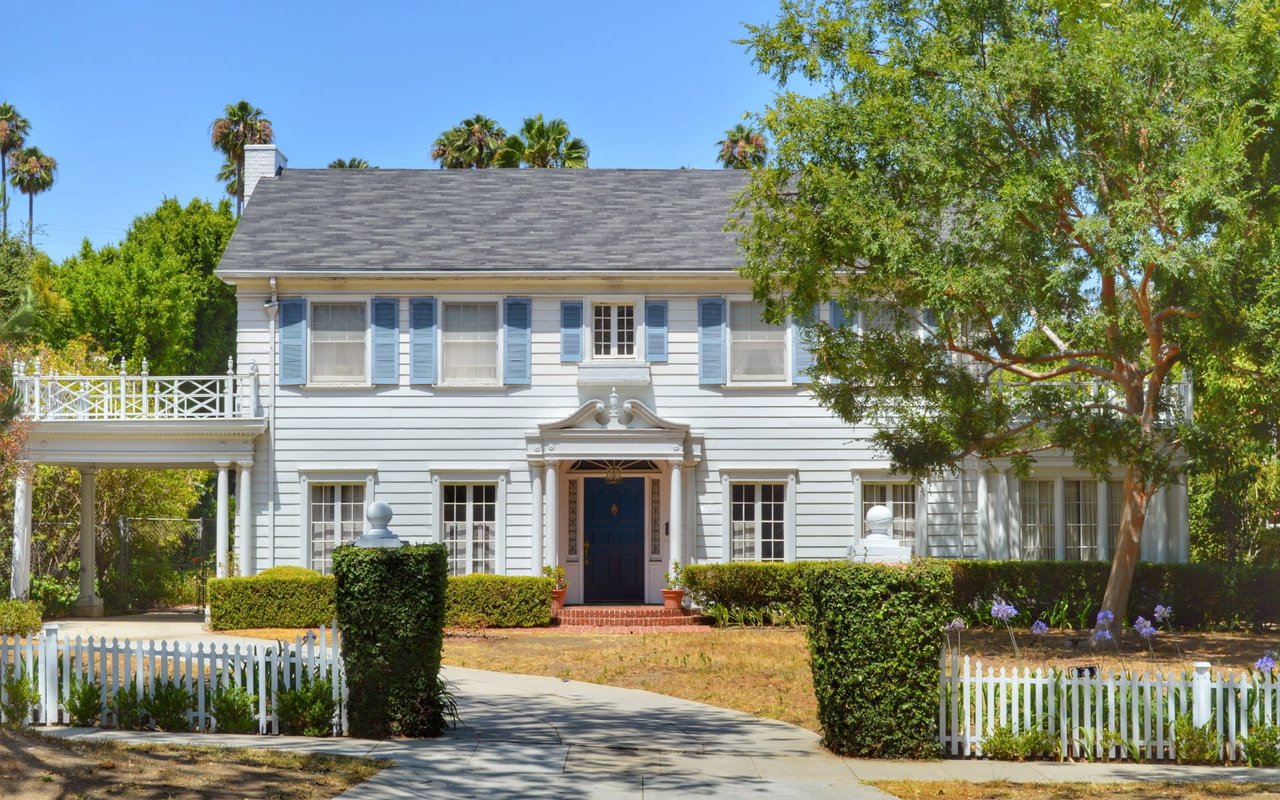 A white house with a blue and white striped shutter on the exterior windows of the house.