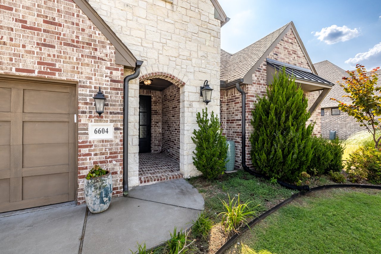 Brick and stone home with an arched entry, attached garage, and landscaped front yard.